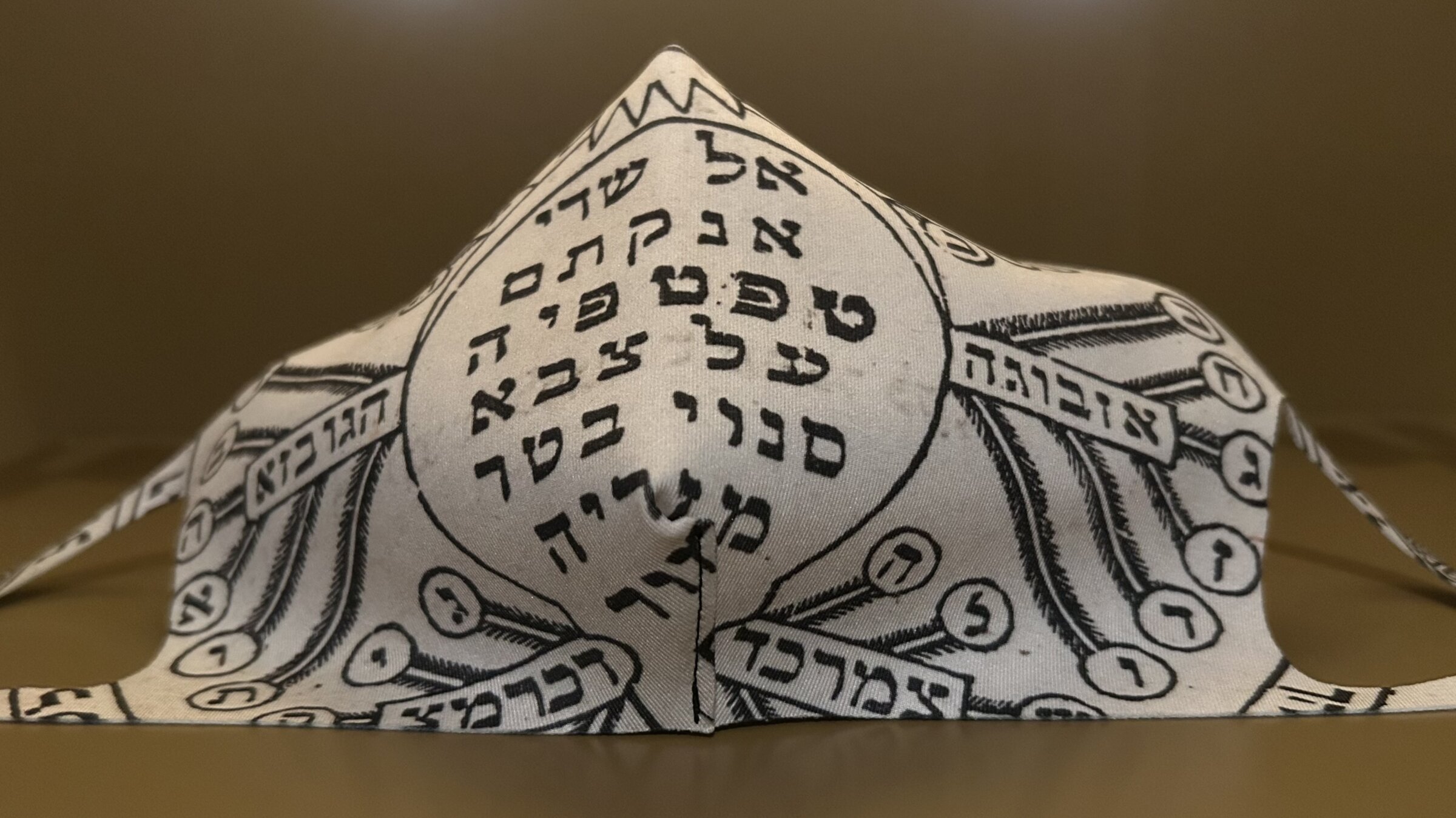 אַ מאַסקע וואָס איז גלײַכצײַטיק אַ קמיע מיט הייליקע אותיות, געשאַפֿן פֿון קען גאָלדמאַן  בעת דער קאָוויד־פּאַנדעמיע, 2020