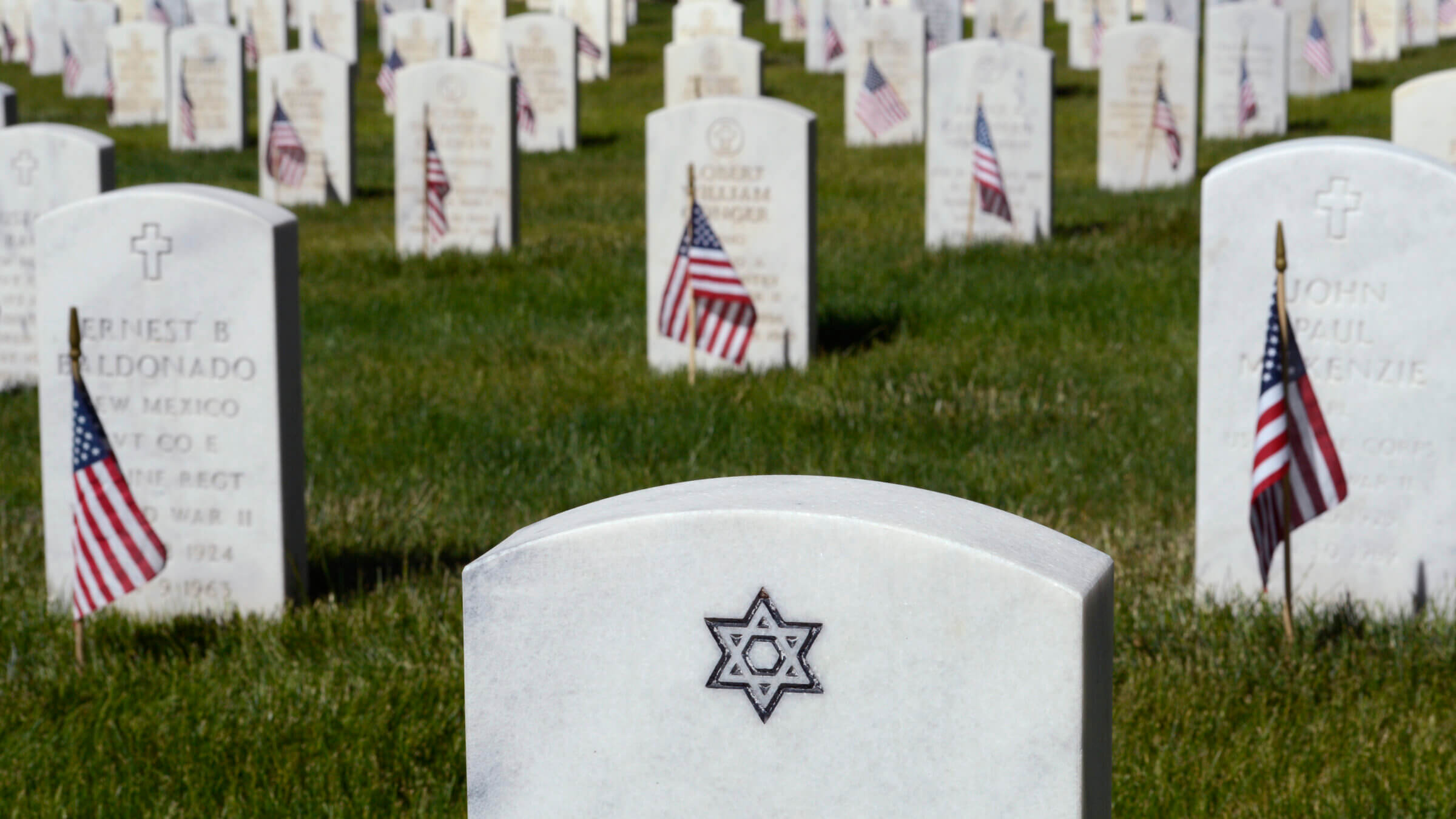 Small American flags adorn the graves of U.S. military veterans, including the grave of a Jewish veteran whose tombstone is embellished with the Star of David, buried at the Santa Fe National Cemetery.