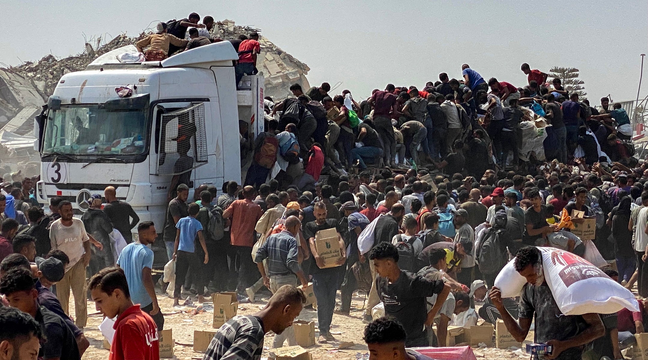 Displaced Palestinians carry food parcels as they raid trucks carrying humanitarian aid in Khan Yunis, in the southern Gaza Strip on August 9, 2025.