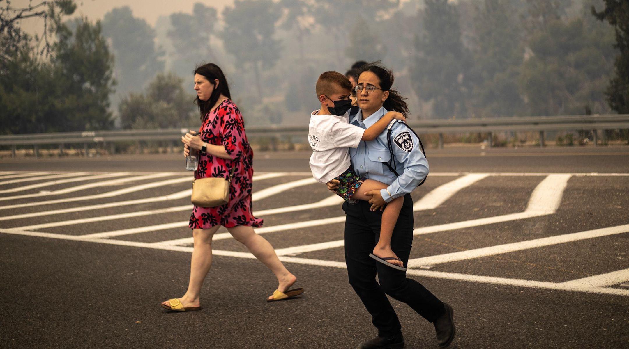 An Israeli police officer evacuates a child from the wildfires. (Israel Police/X)