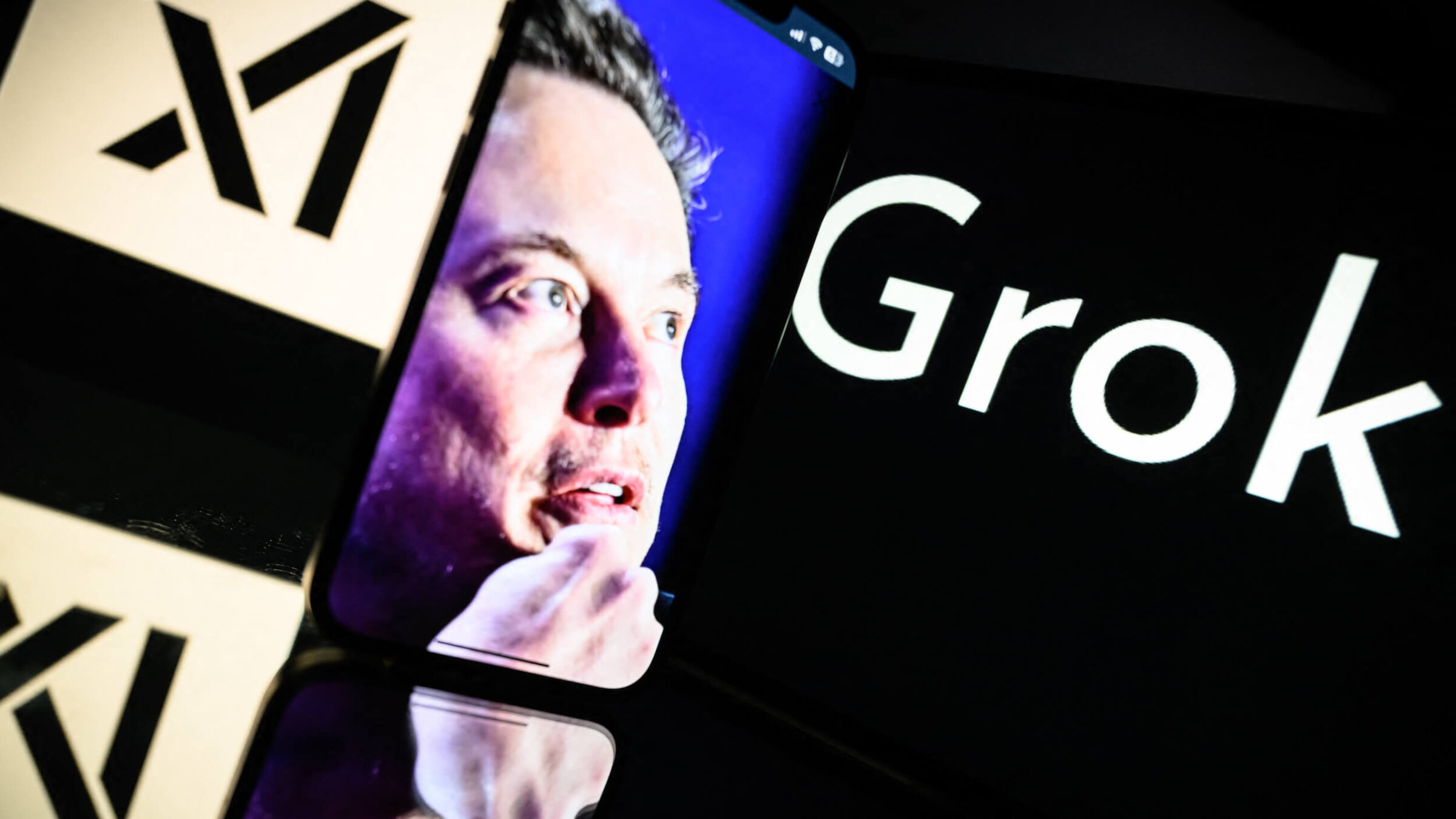 Screens displaying the logo of Grok, a generative artificial intelligence chatbot developed by xAI, and the image of its founder, Elon Musk.