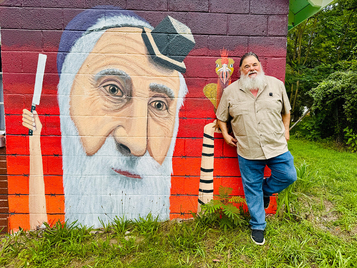 Howard Jaffe next to one section of the mural remembering the history of the Alliance Colony. The painting by Jonathan Blum depicts Isaac Krassenstein, known as the Hasid of Alliance and a kosher butcher.