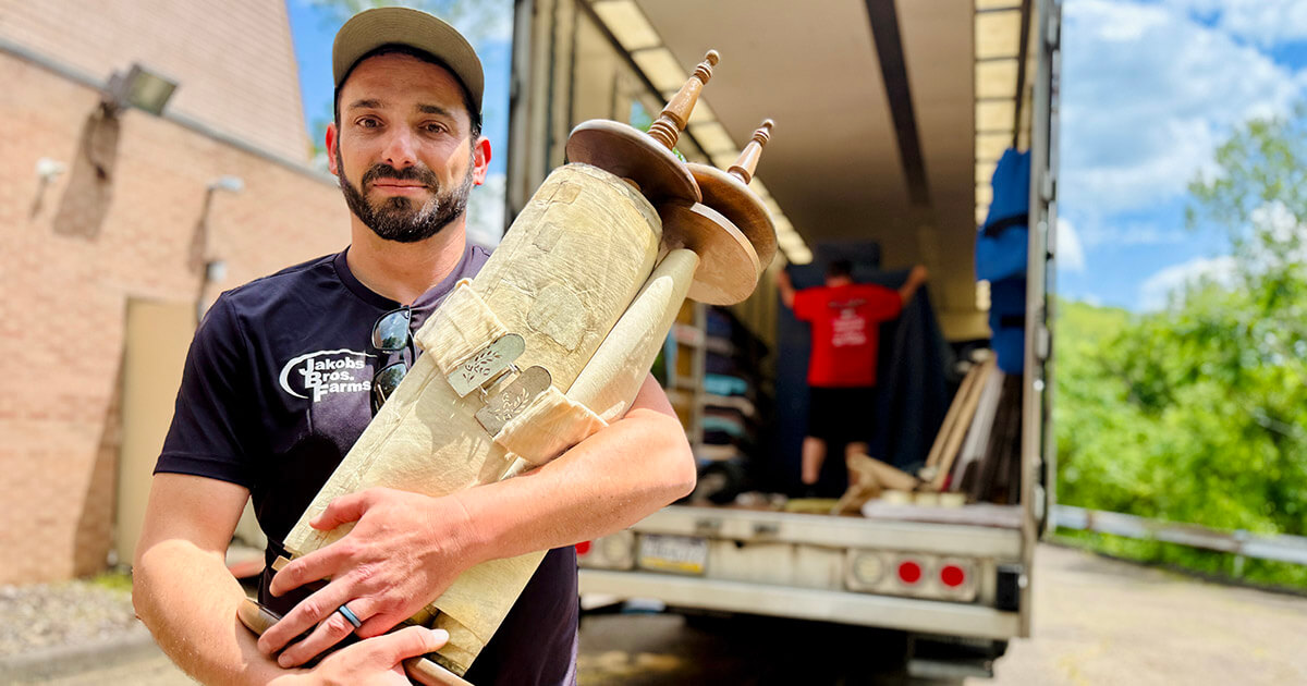 Nik Jakobs holding the Torah donated to him by Temple B'nai Israel in White Oak, Pennsylvania. A moving truck is in the background.